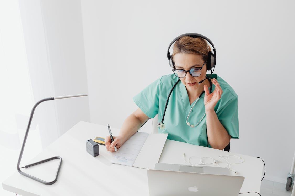 a doctor attending an online call while writing in a notebook