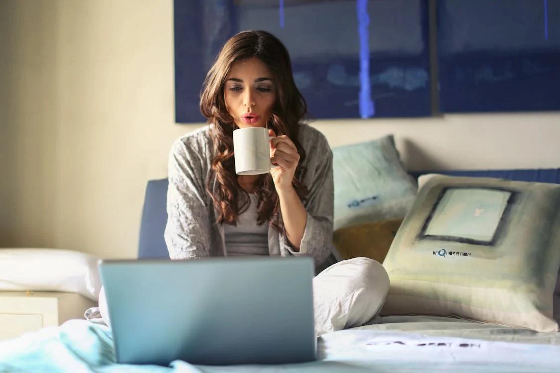 A woman sitting with a laptop, drinking coffee 