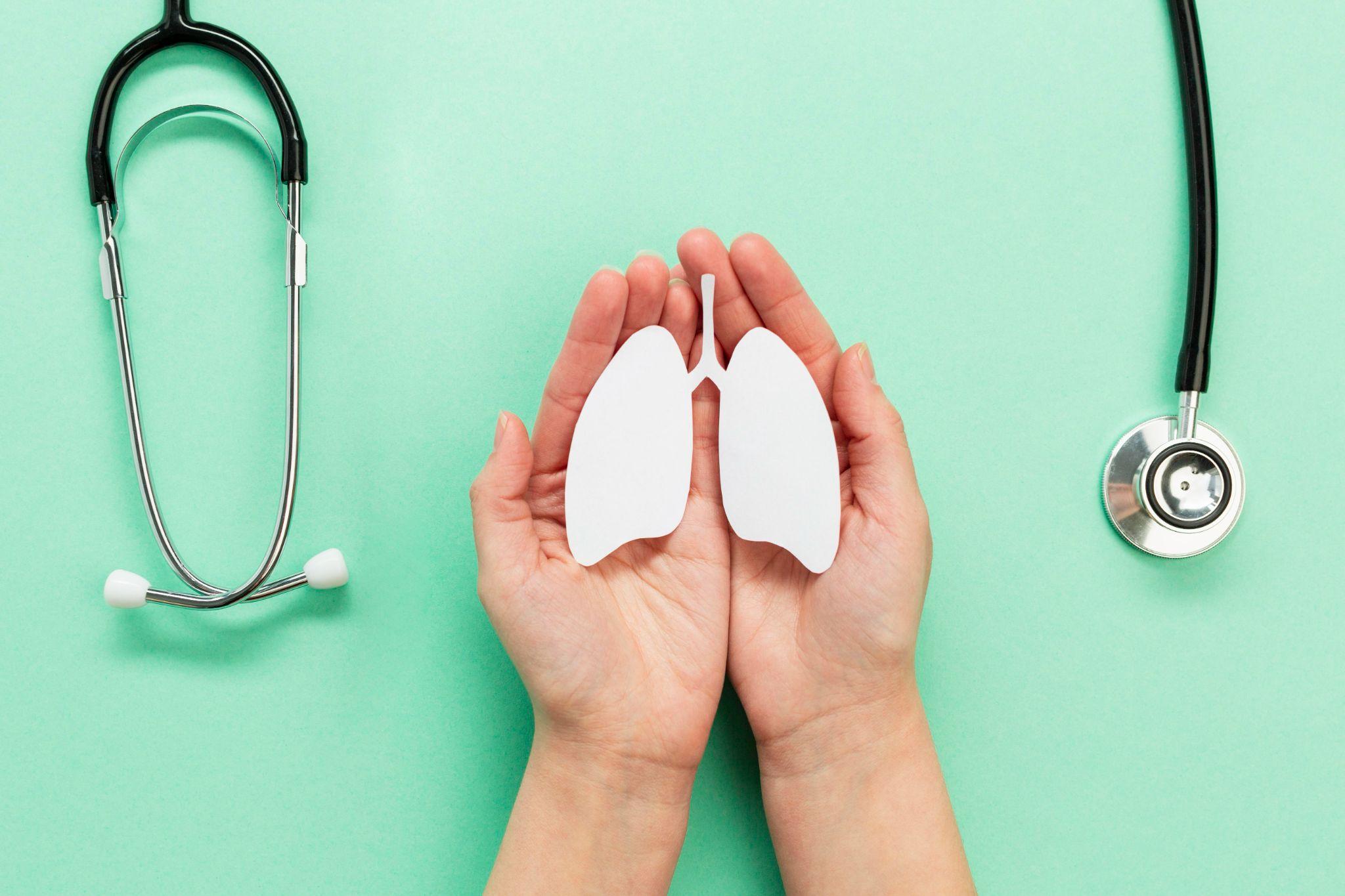 A pair of hands holding a cut-out image of lungs, with a stethoscope placed beside it