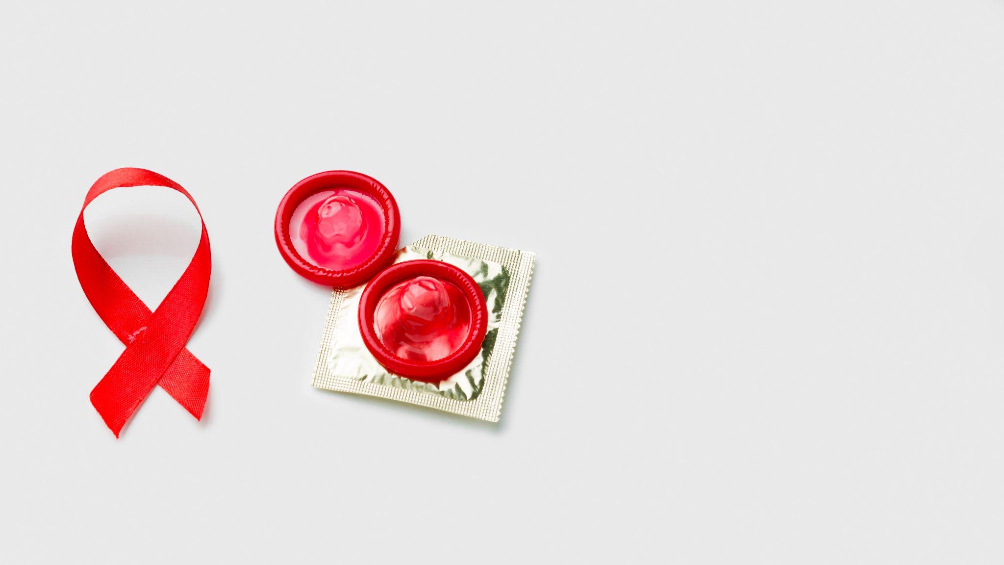 A red awareness ribbon next to two red condoms, symbolizing HIV prevention and safe sex.