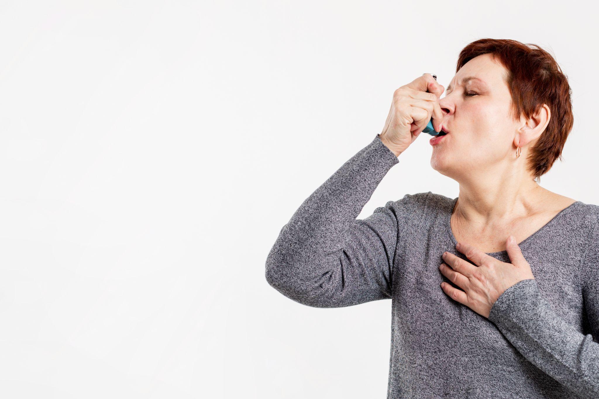 A woman inhaling from an inhaler, standing against a white background