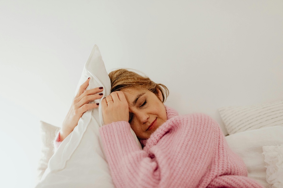 Woman sitting dazed in bed clutching a pillow