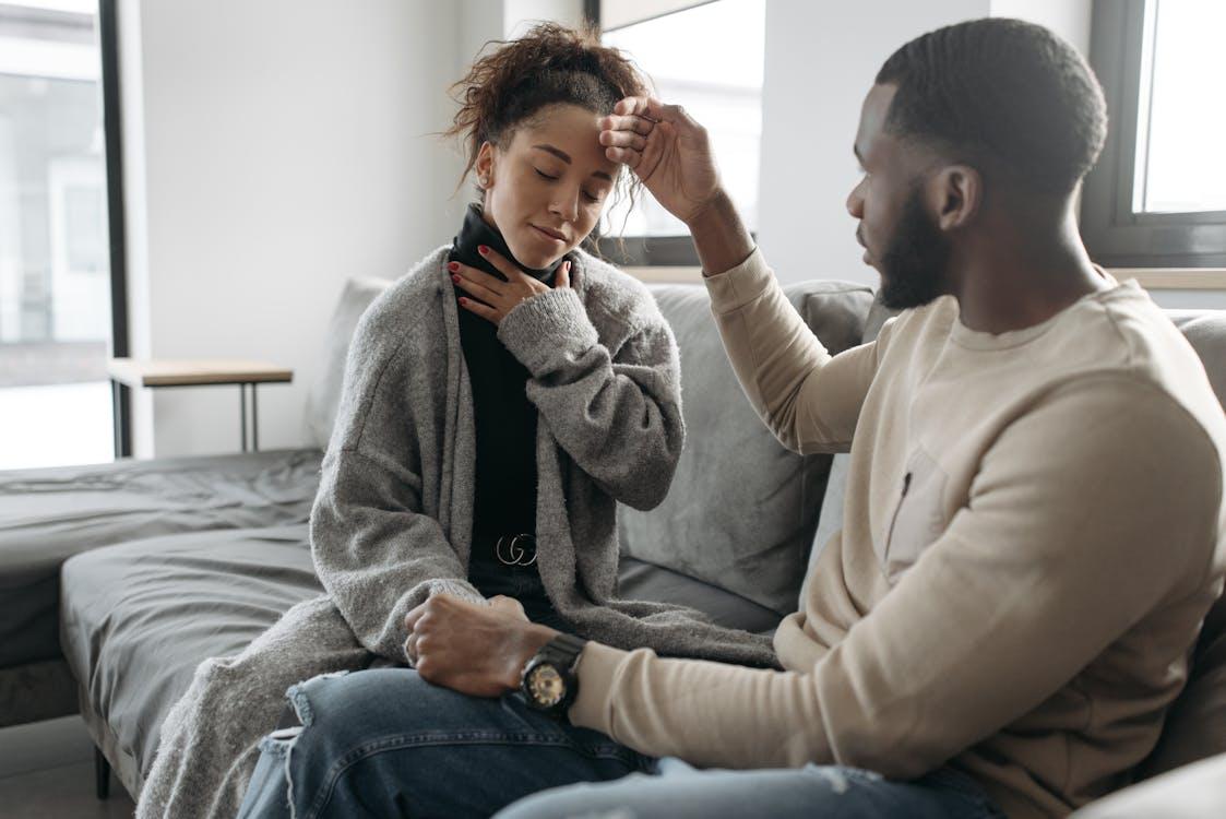 A man checking the temperature of a woman resting in bed, highlighting caregiving responsibilities