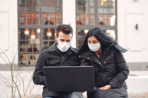 couple in masks using a laptop while traveling in the city