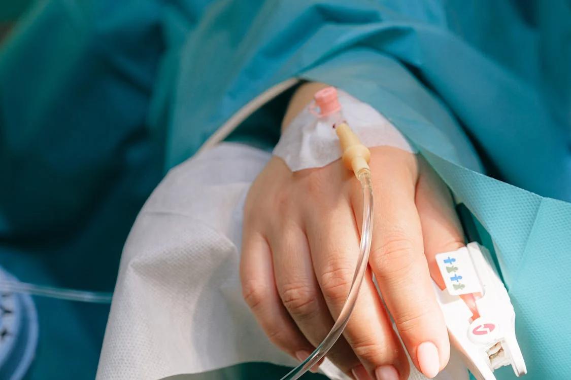 A patient in a hospital bed with an IV line in their arm, indicating a serious health condition