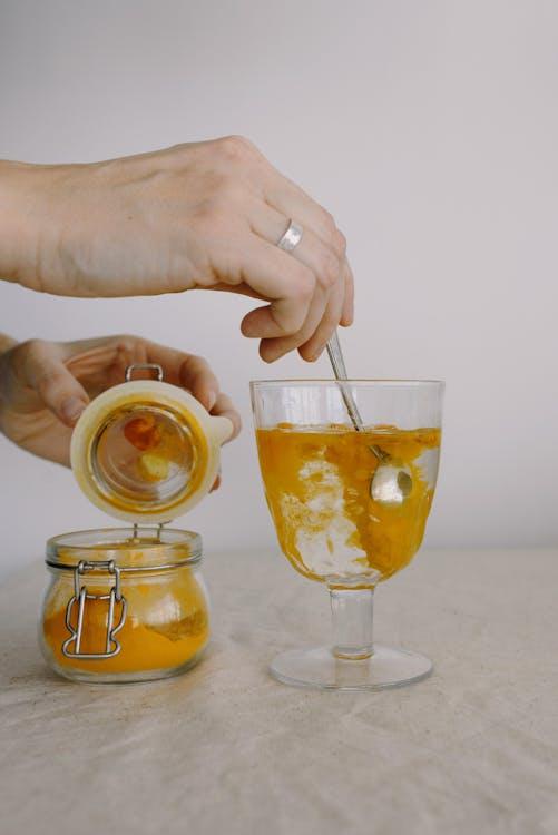 An image of a person’s hands adding turmeric to a glass of hot water