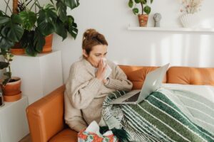 sick woman wiping nose while using laptop on sofa