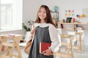 A girl standing in her class with her schoolbag and books