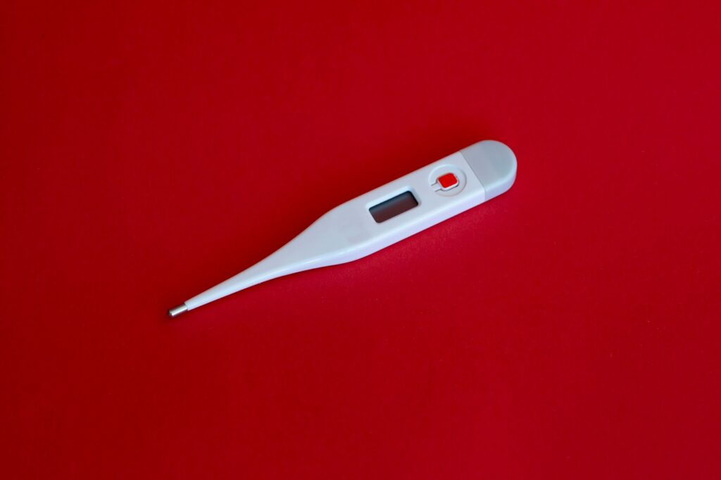 Digital thermometer on red background used to monitor and reduce high fever at home.