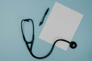 A stethoscope, paper and pen placed on a blue surface