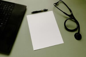 A picture of a paper, stethoscope, pen and laptop