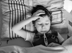 A little boy lying on a bed checking his fever using a digital thermometer