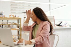 Young woman sitting at a workplace rubbing her forehead while feeling unwell.