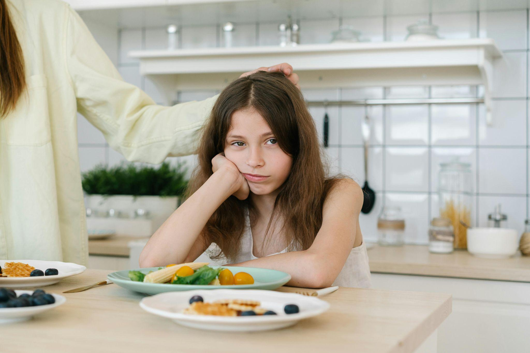 A girl showing low appetite while sitting at a table with untouched food