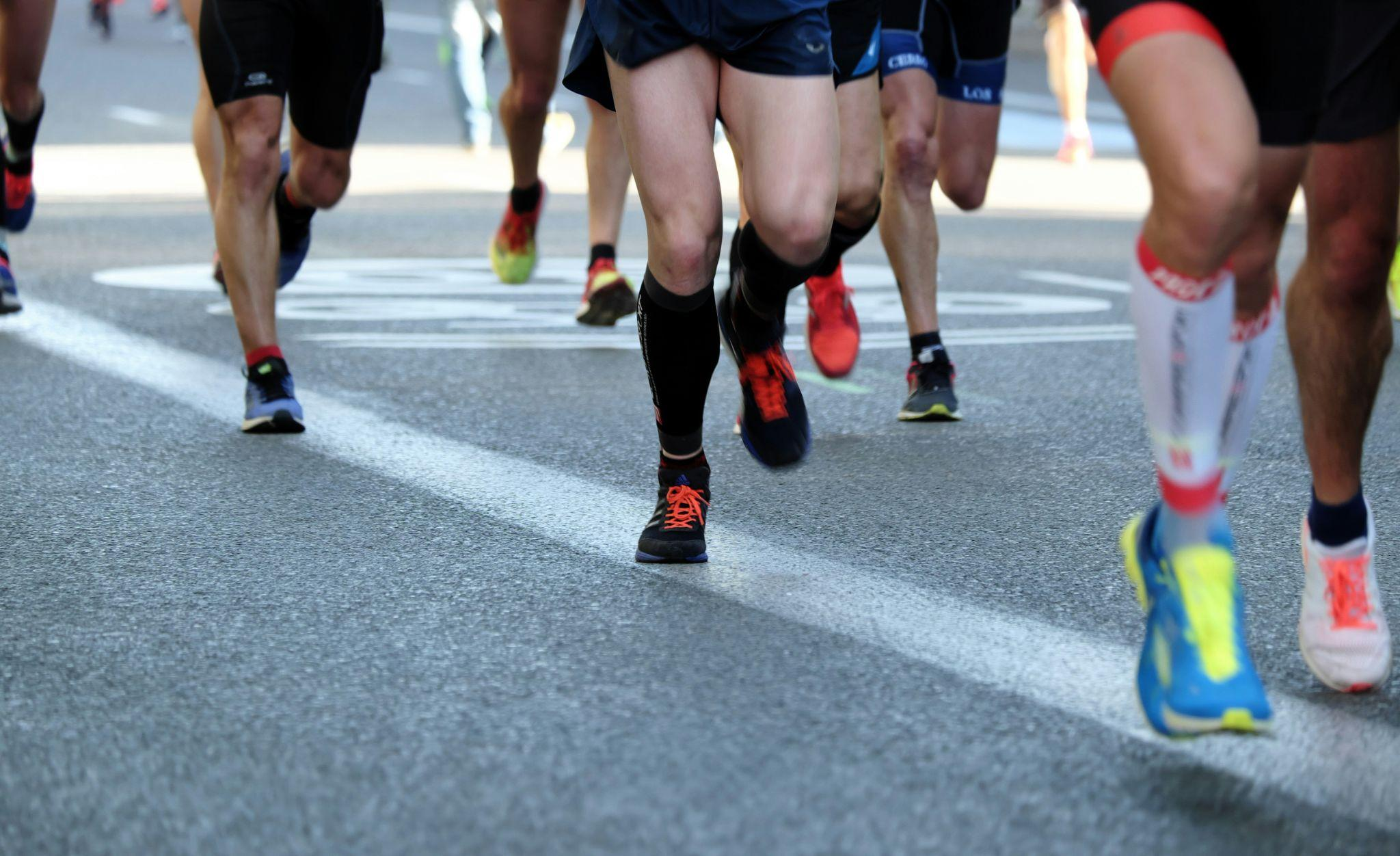 A group of people running during a race with visible legs and shoes.