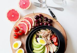Bowl of balanced food with eggs, avocado, vegetables, and fresh fruit.