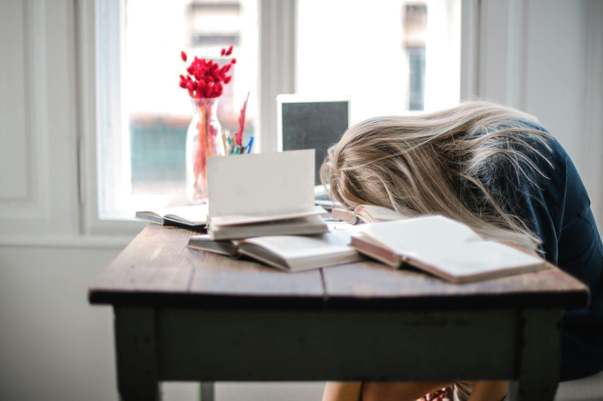 Woman collapsed over a desk surrounded by notebooks.