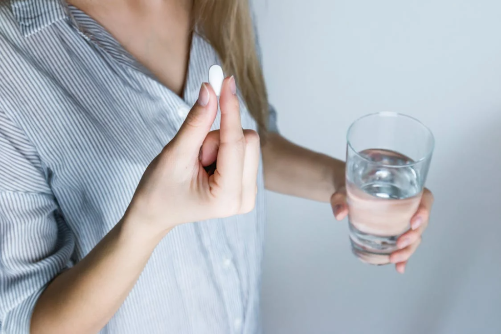 a person holding a glass of water and a pill.