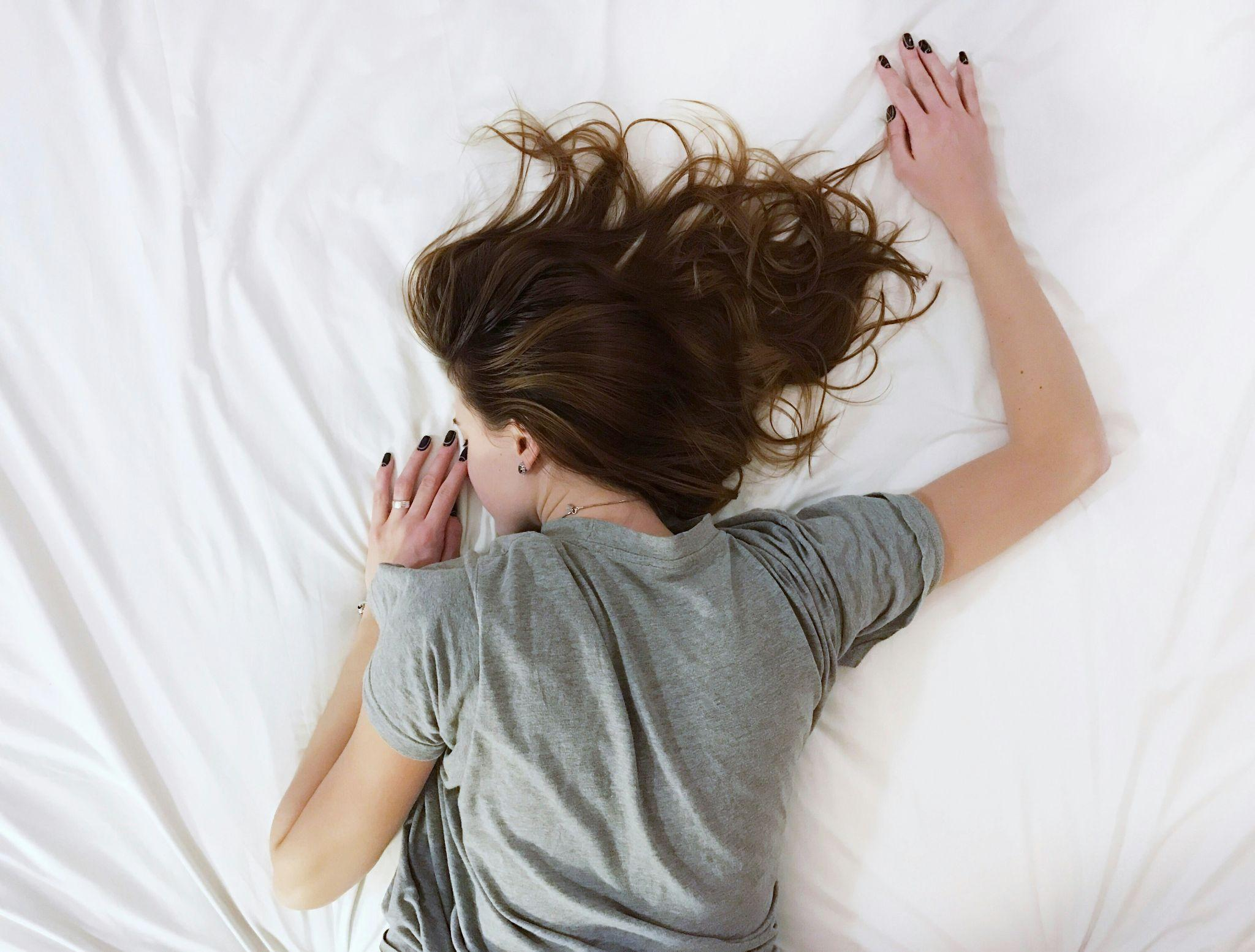 Woman lying face-down on a bed with her arms stretched forward