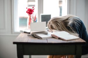 a tired woman with her head down on the desk surrounded by books