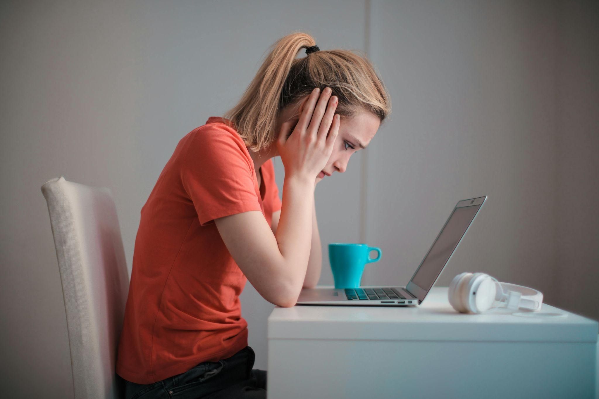Woman holding her head in frustration while working on a laptop.