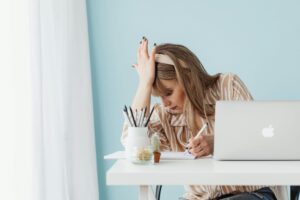 Woman holding her head while writing at a desk, showing visible stress.