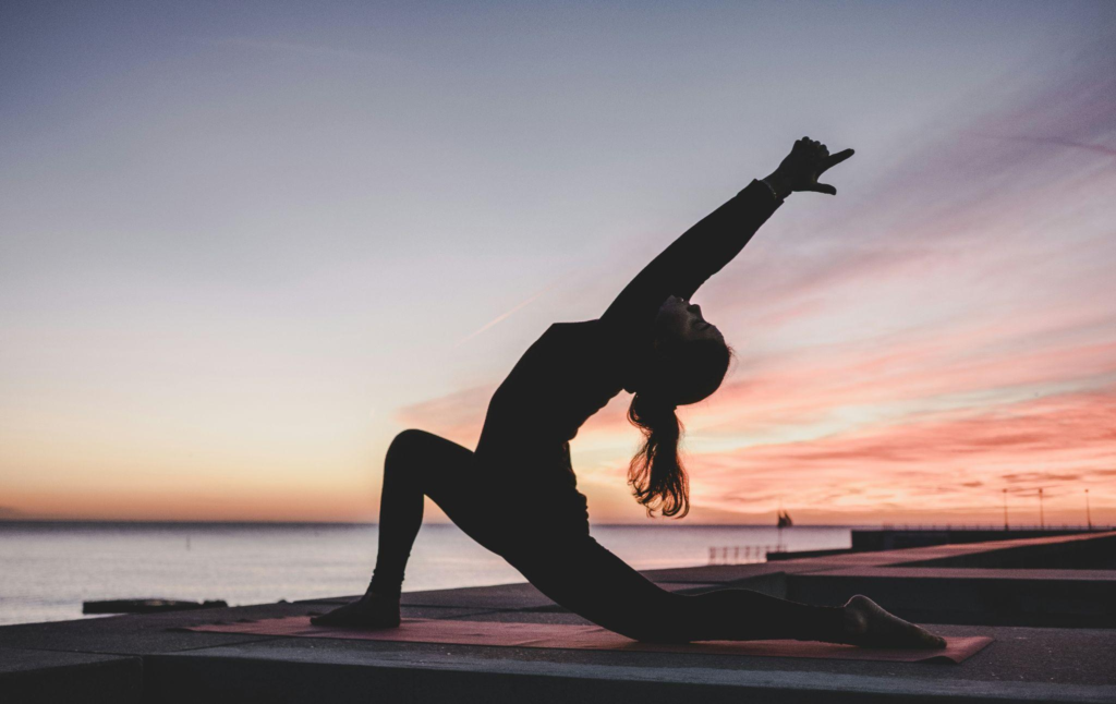 Person stretching outdoors during a sunrise yoga pose.