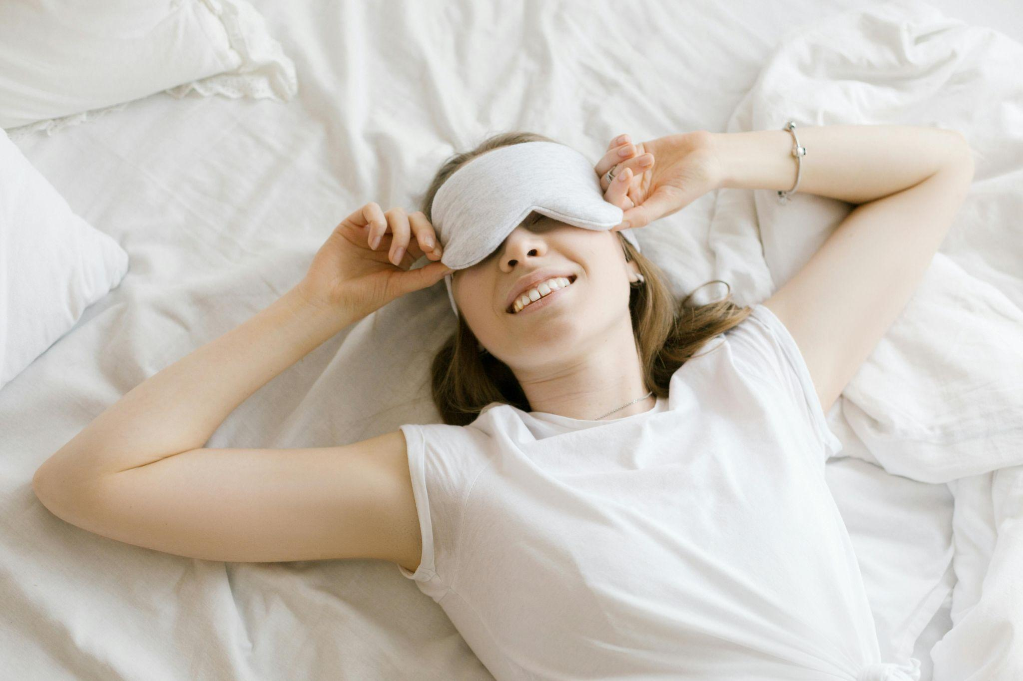 Woman lying in bed with a sleep mask and smiling.