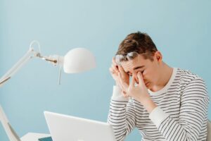 Young man rubbing his eyes in fatigue while working on a laptop.