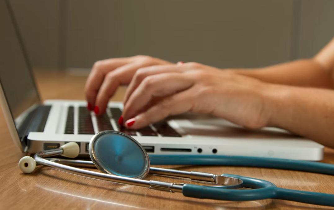 This image shows a doctor working on a laptop with a stethoscope nearby.