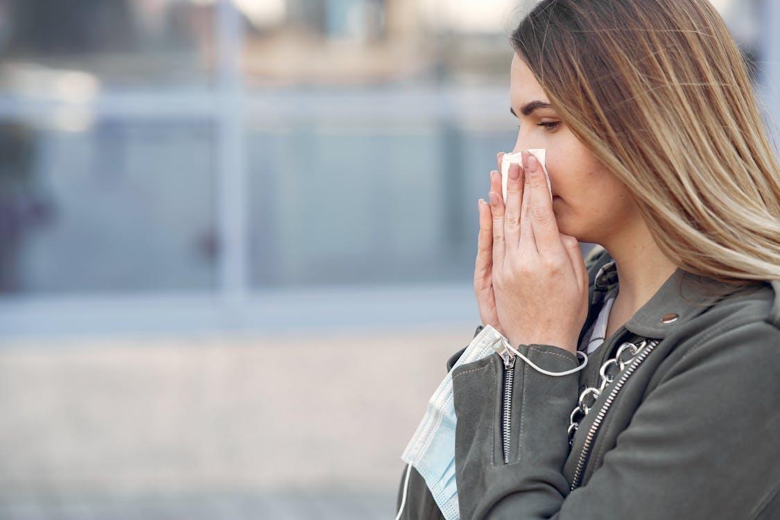 Adult sneezing outdoors while holding a face mask