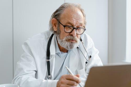 Doctor with a stethoscope around neck writing a doctor’s note while working on a laptop