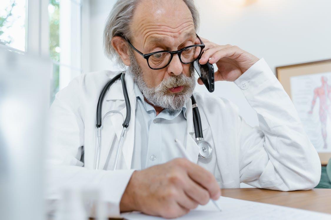 Doctor speaking on the phone while reviewing medical leave documentation.