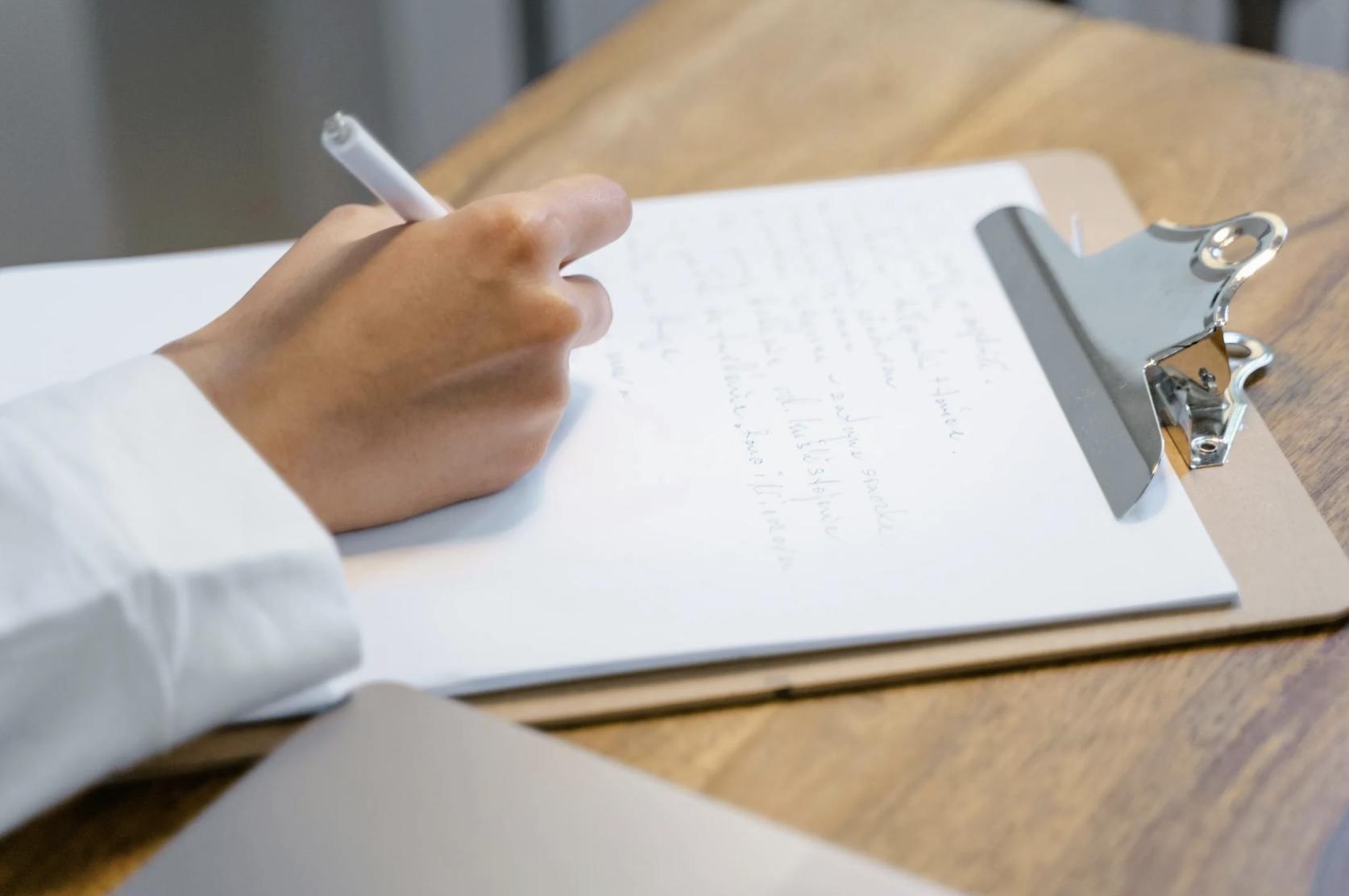 This photo shows a close-up of hands filling out a document on a clipboard.