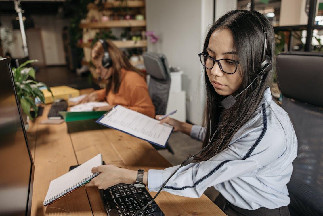 A woman wearing a headset holding a notebook and clipboard at an office desk