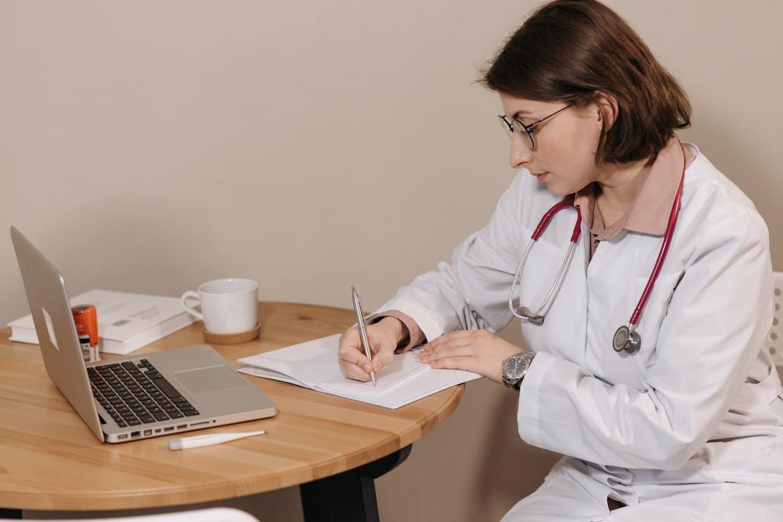 Doctor writing medical documentation during online FMLA certification process for employee leave.