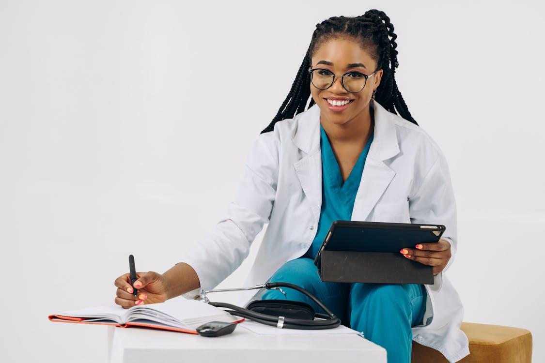 Doctor using a tablet while writing notes for employee medical leave documentation.