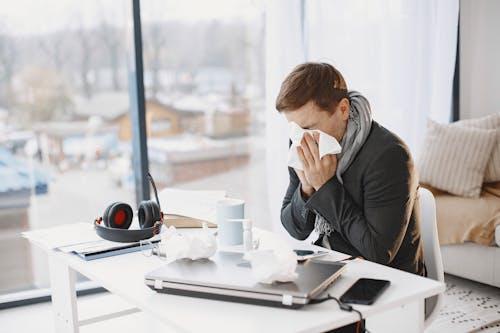 Sick employee sitting at a desk, sneezing while working in an office environment