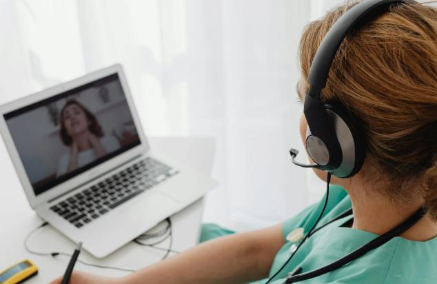 This image shows a woman wearing headphones on a video call with a patient.