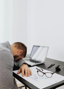 This photo shows a person sitting with head resting on a desk looking tired.