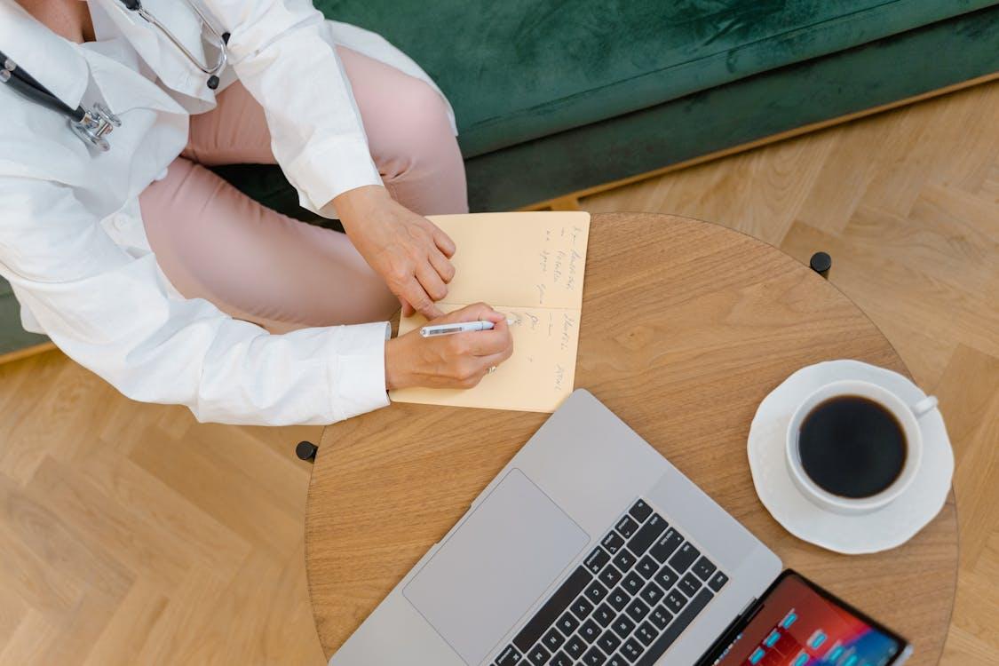 Cropped photo of a doctor writing a note near a laptop