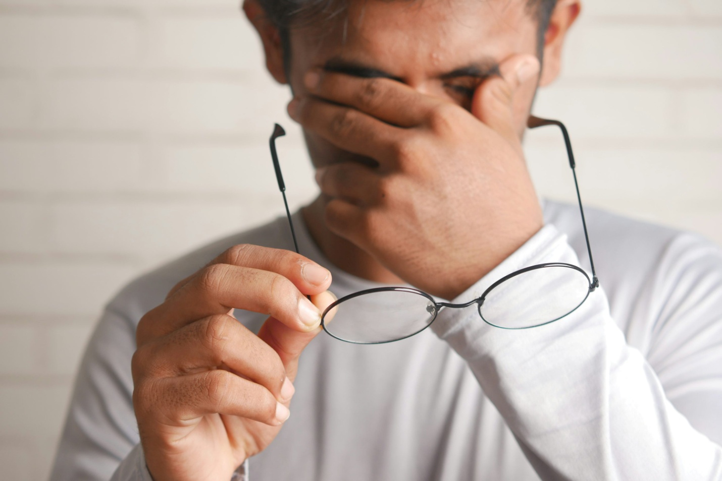 A man rubbing his face while holding his glasses