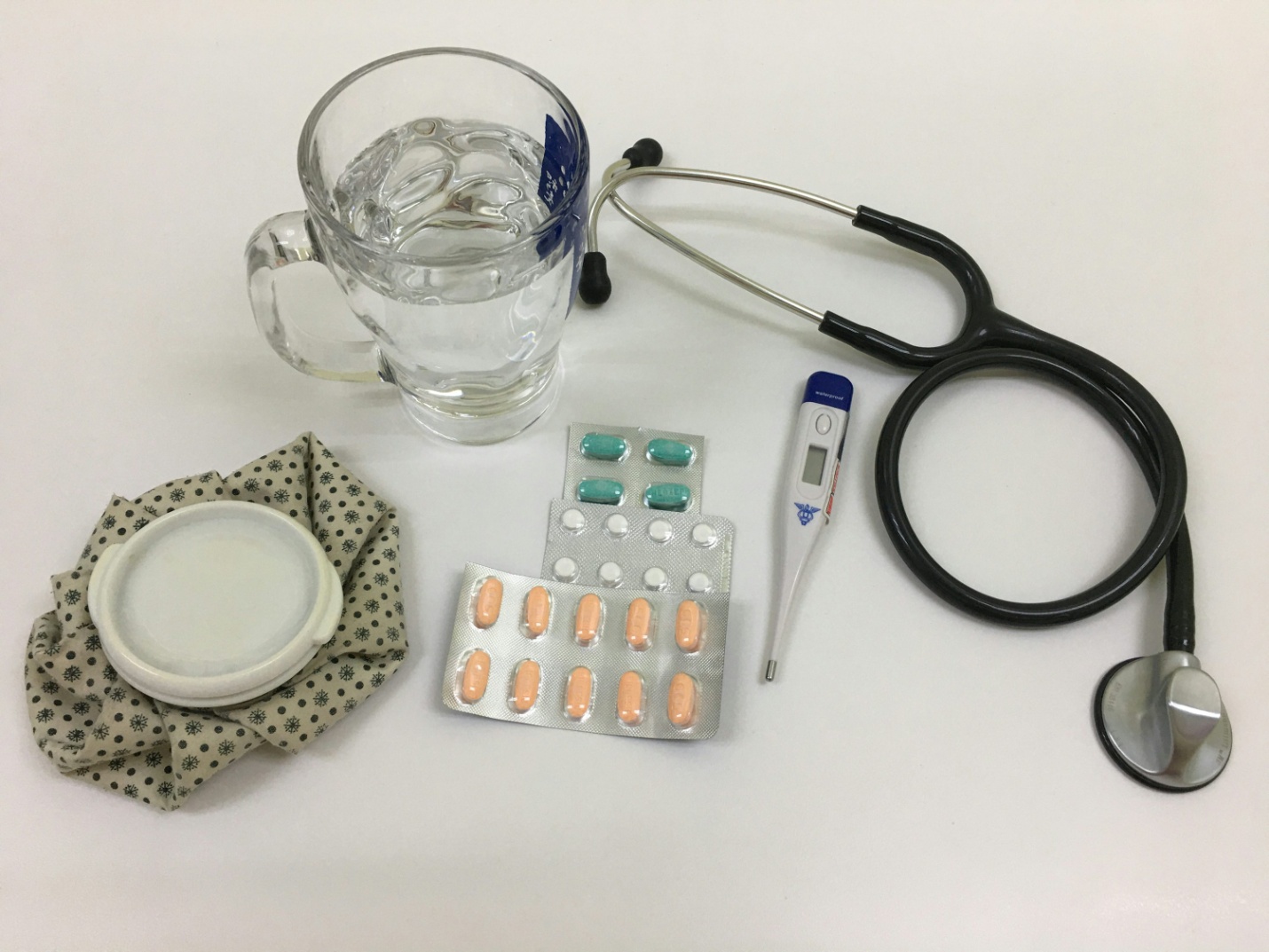 A pile of pills next to a glass of water and a thermometer